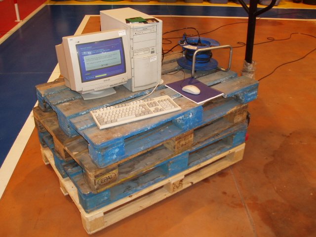 Ordenador de sobremesa con CPU, monitor, teclado y ratón montado sobre unos palets y una transportadora con ruedas